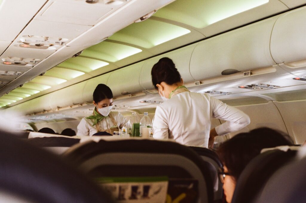 Flight attendants in white uniforms and masks serving passengers onboard a Vietnam airplane.