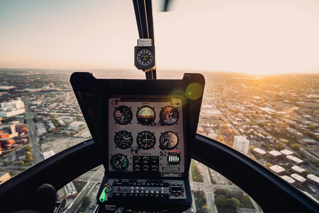 Aerial view from a helicopter cockpit flying over a city during sunset, showcasing the urban landscape.